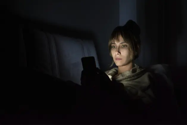 Mujer usando su celular en la oscuridad, ilustrando posibles daños por el uso excesivo del celular durante la noche.