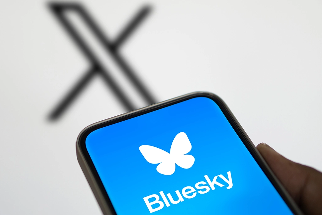 Un teléfono con la imagen de la nueva red Bluesky que gana terreno y de fondo el logo de X, la red con la que compite.
