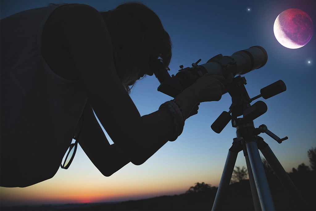 Sombra de un joven mirando en su telescopio el eclipse total de luna