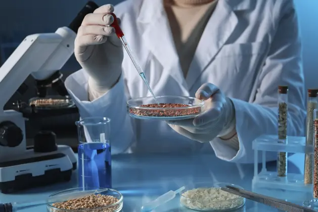 Estudiante de ingeniería bioquímica trabajando en un laboratorio, analizando muestras con microscopio y tubos de ensayo. Carrera científica con amplio campo laboral.