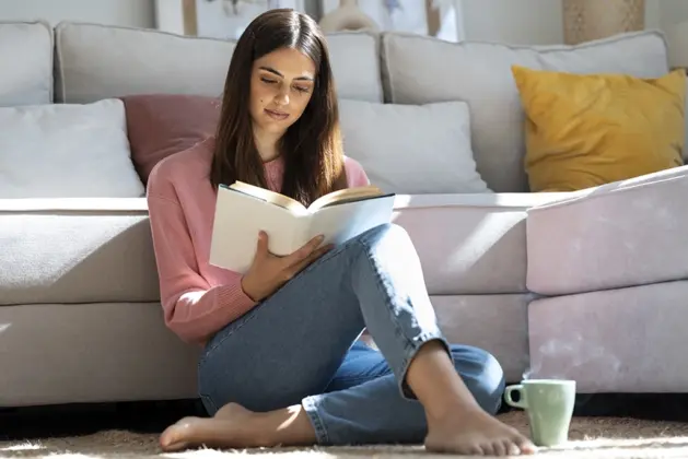 Joven leyendo en la sala de su casa a las autoras que explican conceptos del feminismo