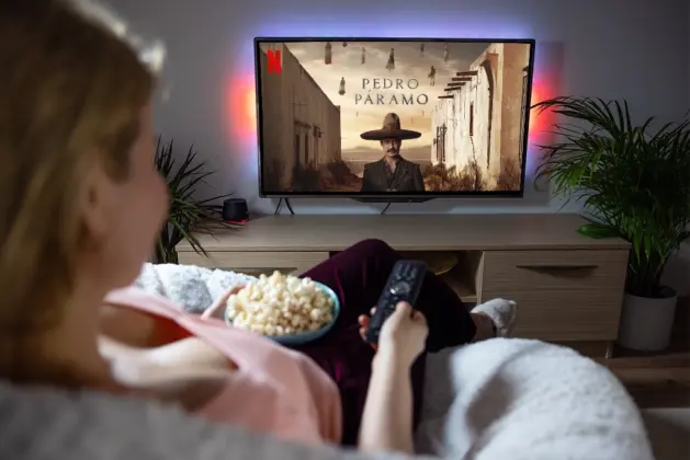 Persona viendo "Pedro Páramo en Netflix" en una pantalla, mientras disfruta de un tazón de palomitas en casa.