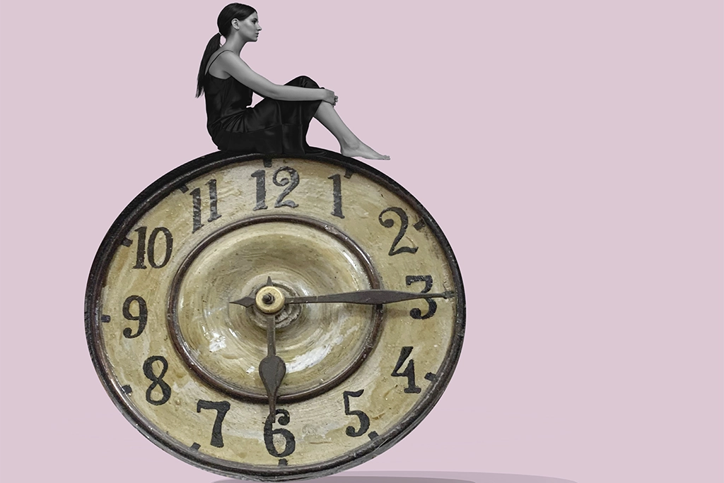 Mujer reflexiva sentada sobre un reloj antiguo, representando la conexión entre el tiempo y la edad mental.