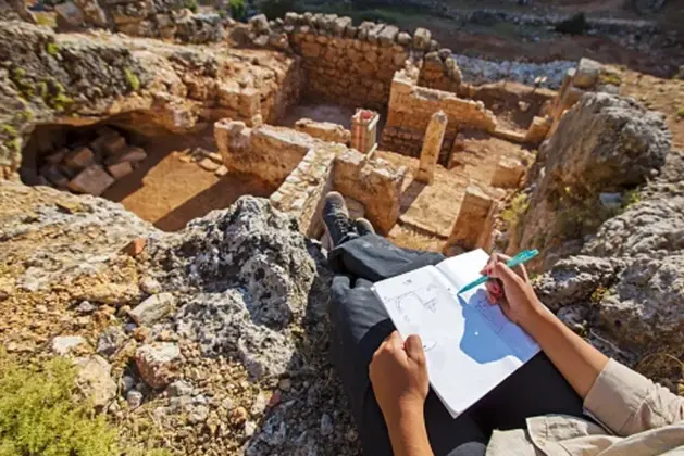Joven arqueólogo en yacimiento, sonriendo mientras sostiene un antiguo artefacto descubierto durante una excavación, al atardecer
