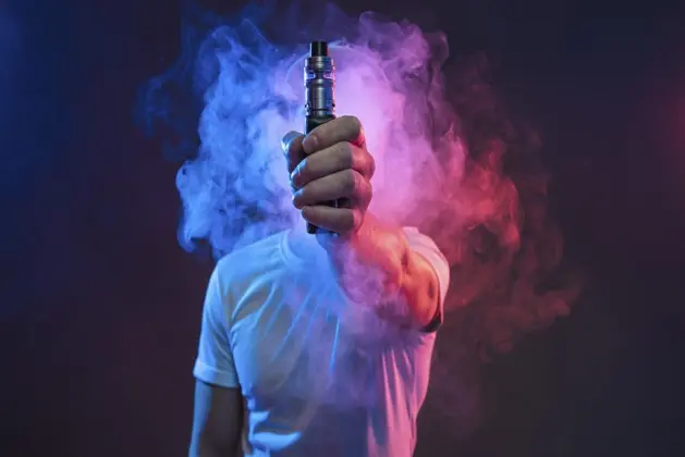 Joven con humo alrededor mostrando un uno de los tipos de vapeadores, simbolizando que Vapear puede ser una adicción y es nocivo para la salud,