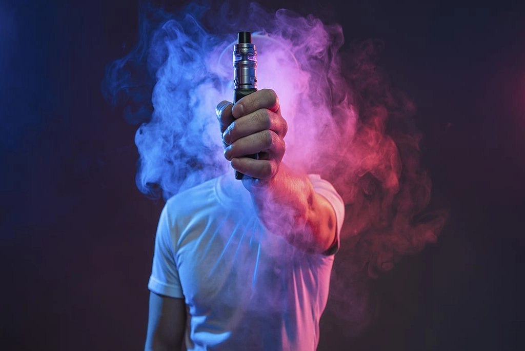 Joven con humo alrededor mostrando un uno de los tipos de vapeadores, simbolizando que Vapear puede ser una adicción y es nocivo para la salud,