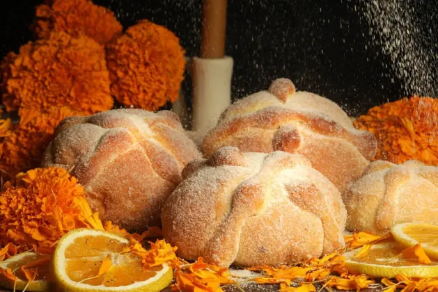 Pan de muerto tradicional mexicano sobre una ofrenda, mostrando su forma circular, la esfera central que simula un cráneo y las tiras de masa que representan huesos, ilustrando el ancestral origen del pan de muerto.