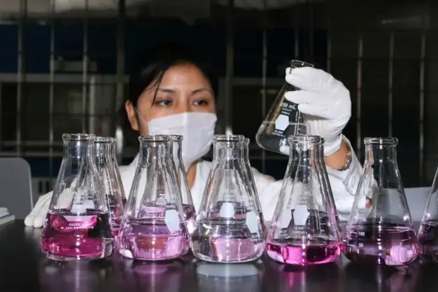 fotografía de una joven estudiante de la ingeniería biológica con cubrebocas y guantes, sosteniendo matraces