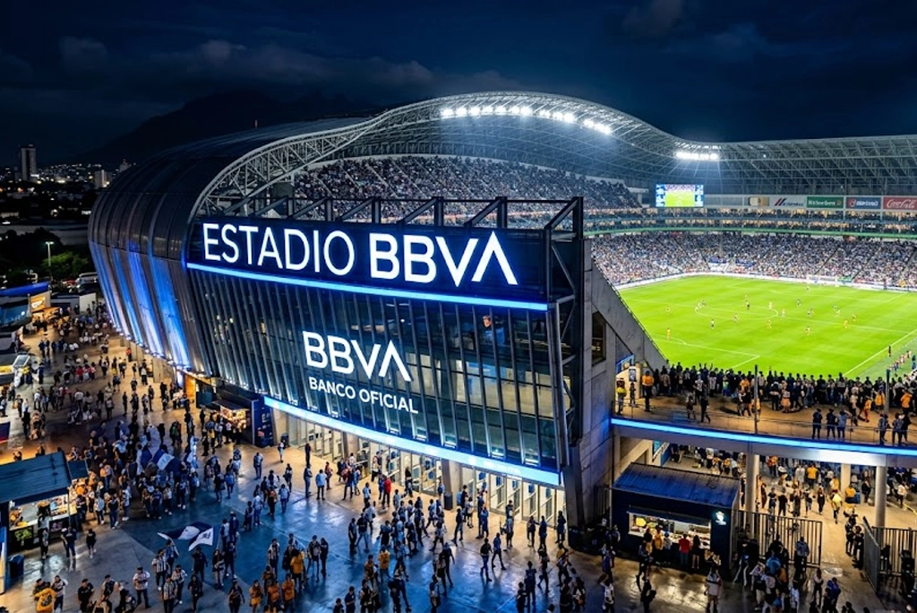 Estadio con nombre de banco iluminado durante un partido nocturno, mostrando la fachada del recinto deportivo con el logotipo de la institución financiera visible en primer plano.