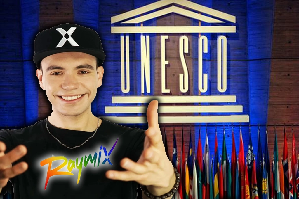 Joven artista Raymix sonriente frente a micrófono en auditorio universitario, con logos de UNESCO y ONU México al fondo, estudiantes diversos escuchando atentos; representa el programa de inclusión LGBTIQ UNESCO en México.